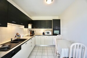 Una cucina compatta con mobili bianchi, un piano di lavoro nero, un forno a microonde e un lavandino.
