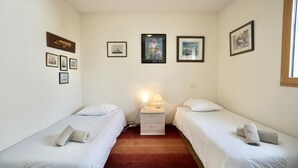 Een kamer met twee eenpersoonsbedden, een nachtkastje met een lamp en ingekaderde foto’s aan de muur.