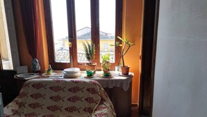 A room with a bed covered in a patterned bedspread, a small table with plates and a potted plant, and a window with curtains. - Casa Vacanze Relax Etna With Stunning Natural Beauty View (Giarre)
