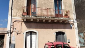 A two-story building with a balcony, a car parked in front, and a door with a number plate. - Casa Vacanze Relax Etna With Stunning Natural Beauty View (Giarre)