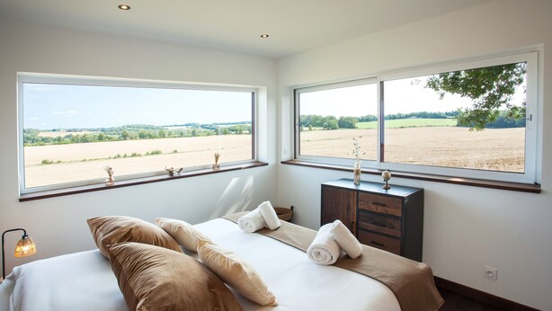 Un dormitorio con una cama grande, dos ventanas, un aparador y una lámpara de noche.