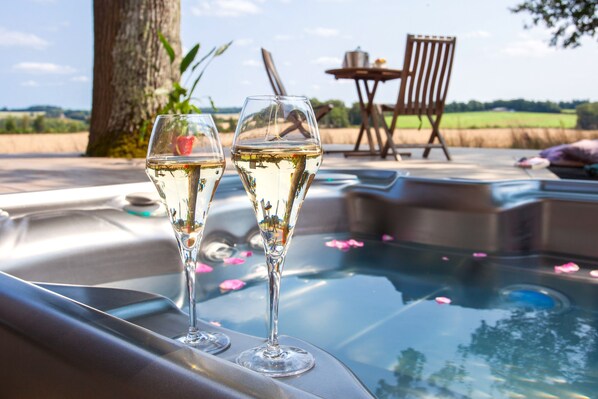 Two glasses of white wine on a table near a hot tub with a chair and table in the background.
