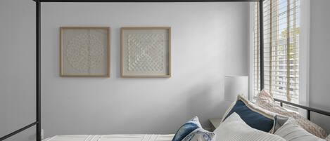 Una camera da letto con struttura letto in metallo, una finestra con persiane e due opere d'arte incorniciate appese al muro.