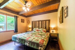 Ein Schlafzimmer mit Holzboden, einem Bett mit Steppdecke, zwei Nachttischen mit Lampen und einem Fenster mit Vorhängen.