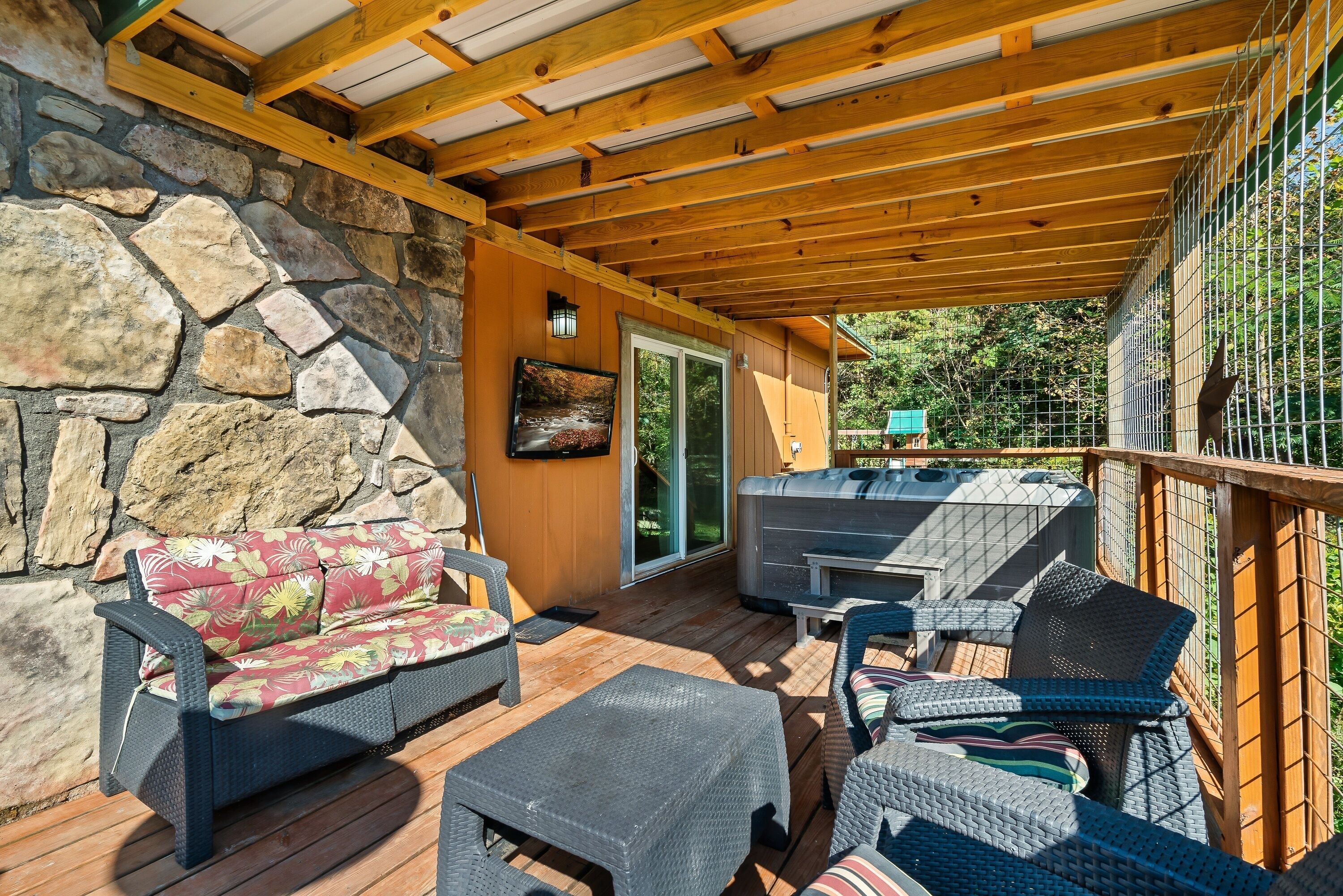 Une terrasse extérieure avec des murs en pierre, des poutres en bois, des meubles en osier et un espace barbecue.