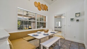 Un coin repas avec une table blanche, un banc et une fenêtre donnant sur un jardin.