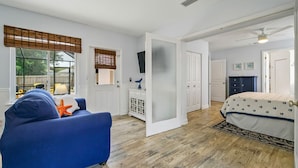Une chambre à coucher avec un lit, un canapé bleu orné d’un coussin en forme d’étoile de mer, une commode blanche et une porte donnant sur une autre pièce.