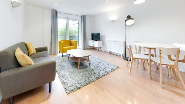 A modern living room with a sofa, a yellow chair, a dining table with chairs, a TV, and a floor lamp. - Still Life Clerkenwell Deluxe (London)