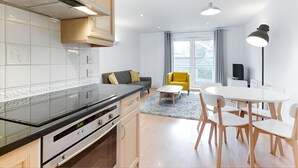 A modern kitchen with a black countertop and stainless steel appliances, a dining area with a white table and chairs, and a sofa with yellow cushions. - Still Life Clerkenwell Deluxe (London)