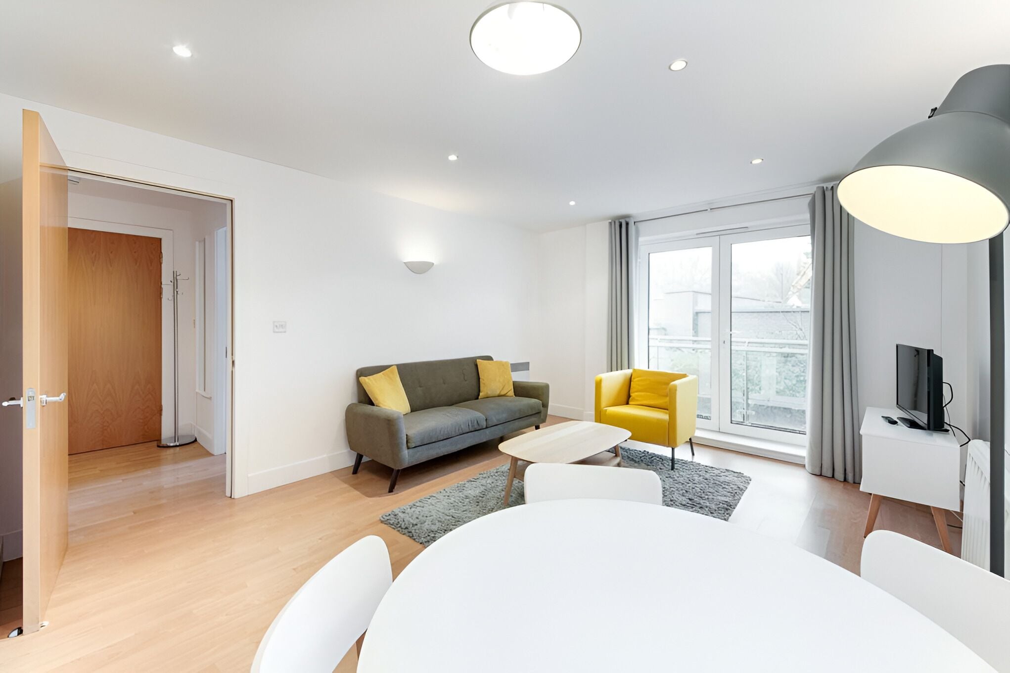 A modern living room with a grey sofa, yellow armchair, and a dining table.