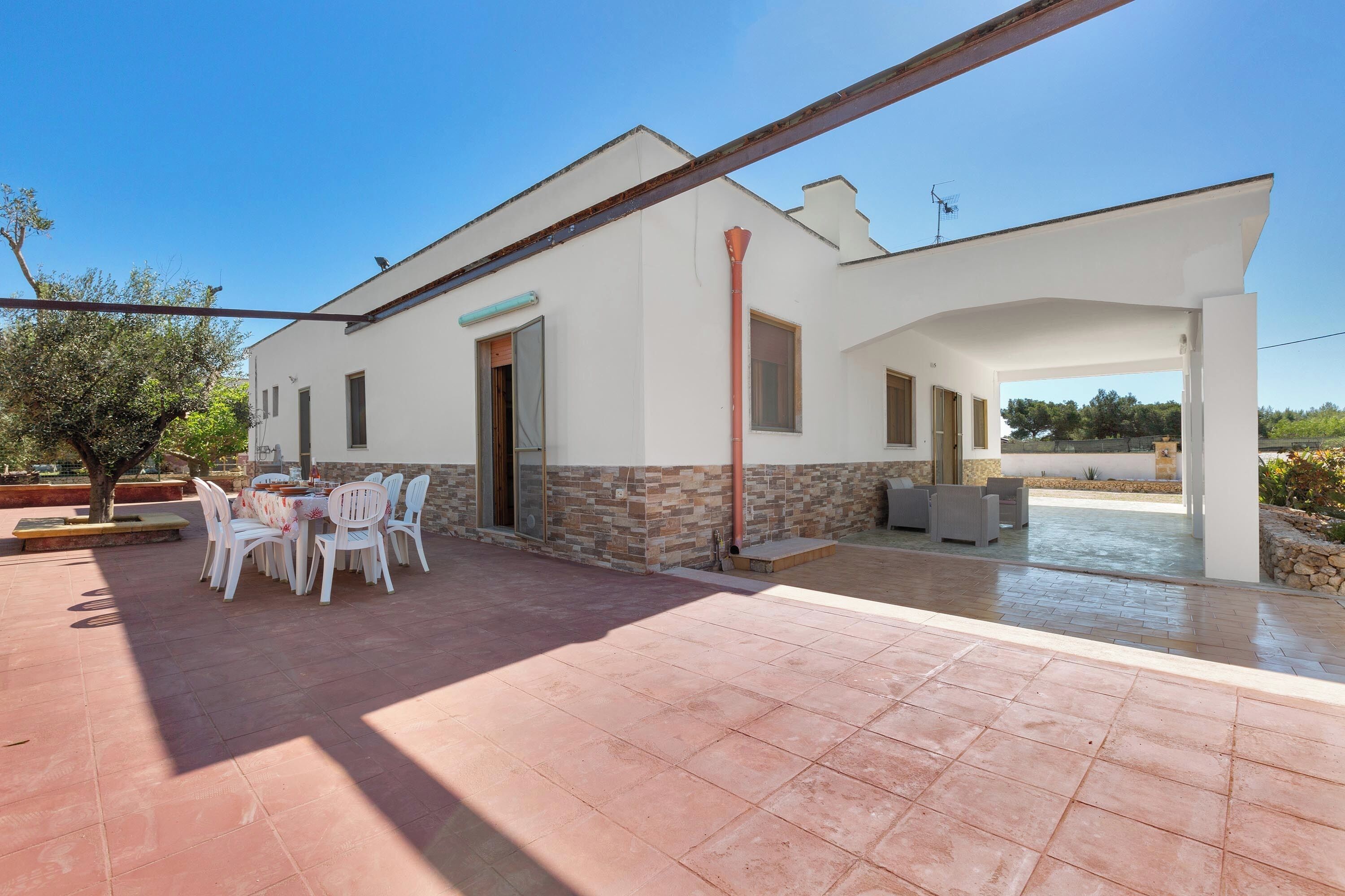 A modern house with a patio, a dining area with white chairs, and a covered outdoor space.