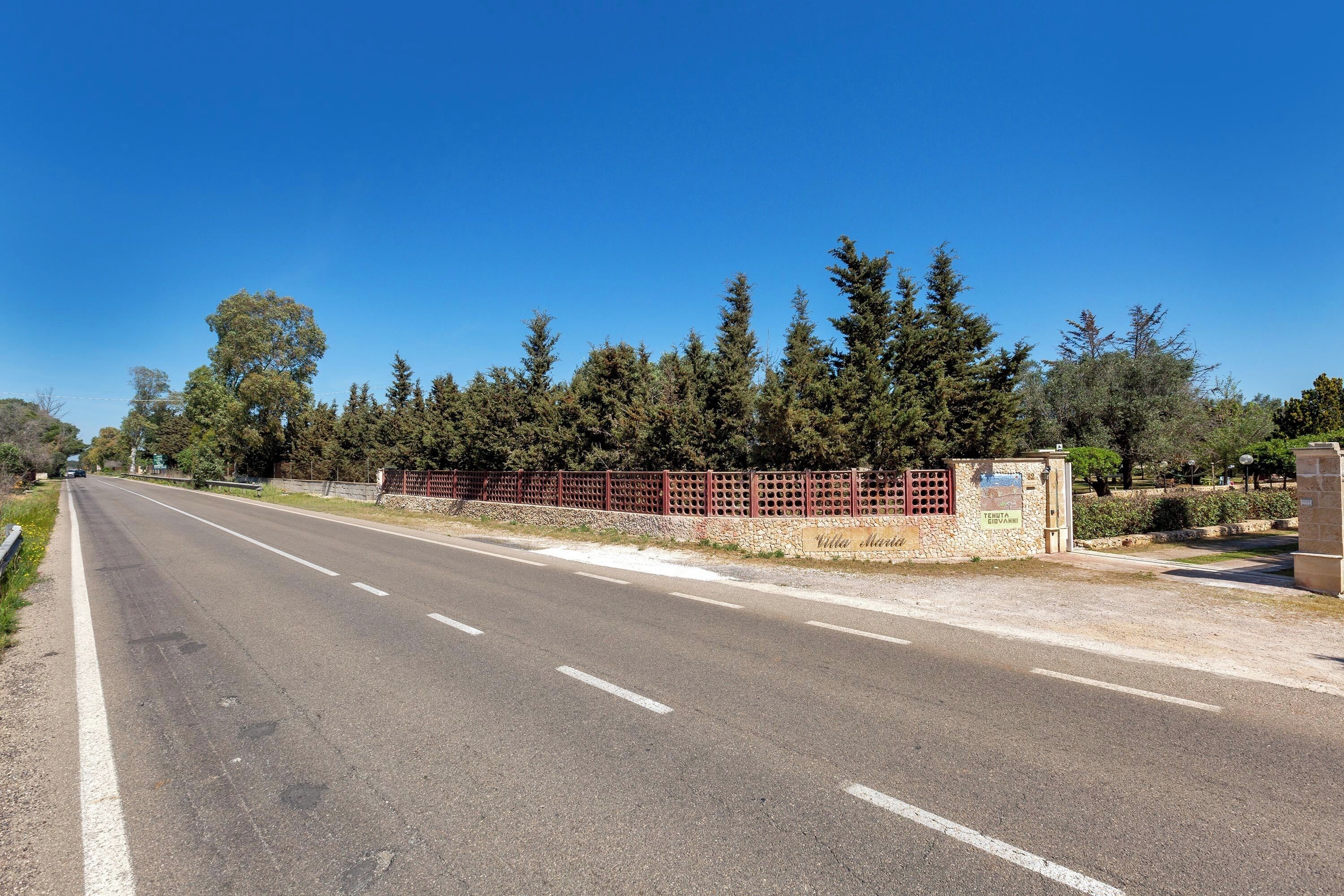 A road with a stone wall and trees on the side.