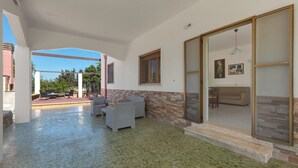 Ein überdachter Patio-Bereich mit Gartenmöbeln, einem Fliesenboden aus Stein und Blick ins Freie.