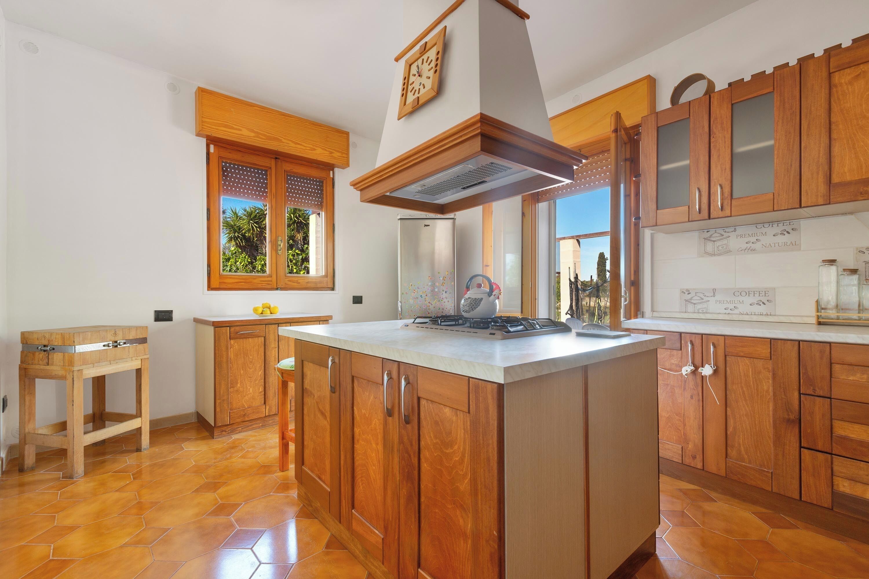 A kitchen with wooden cabinets, a central island, a built-in stove, and a window with a view of greenery.