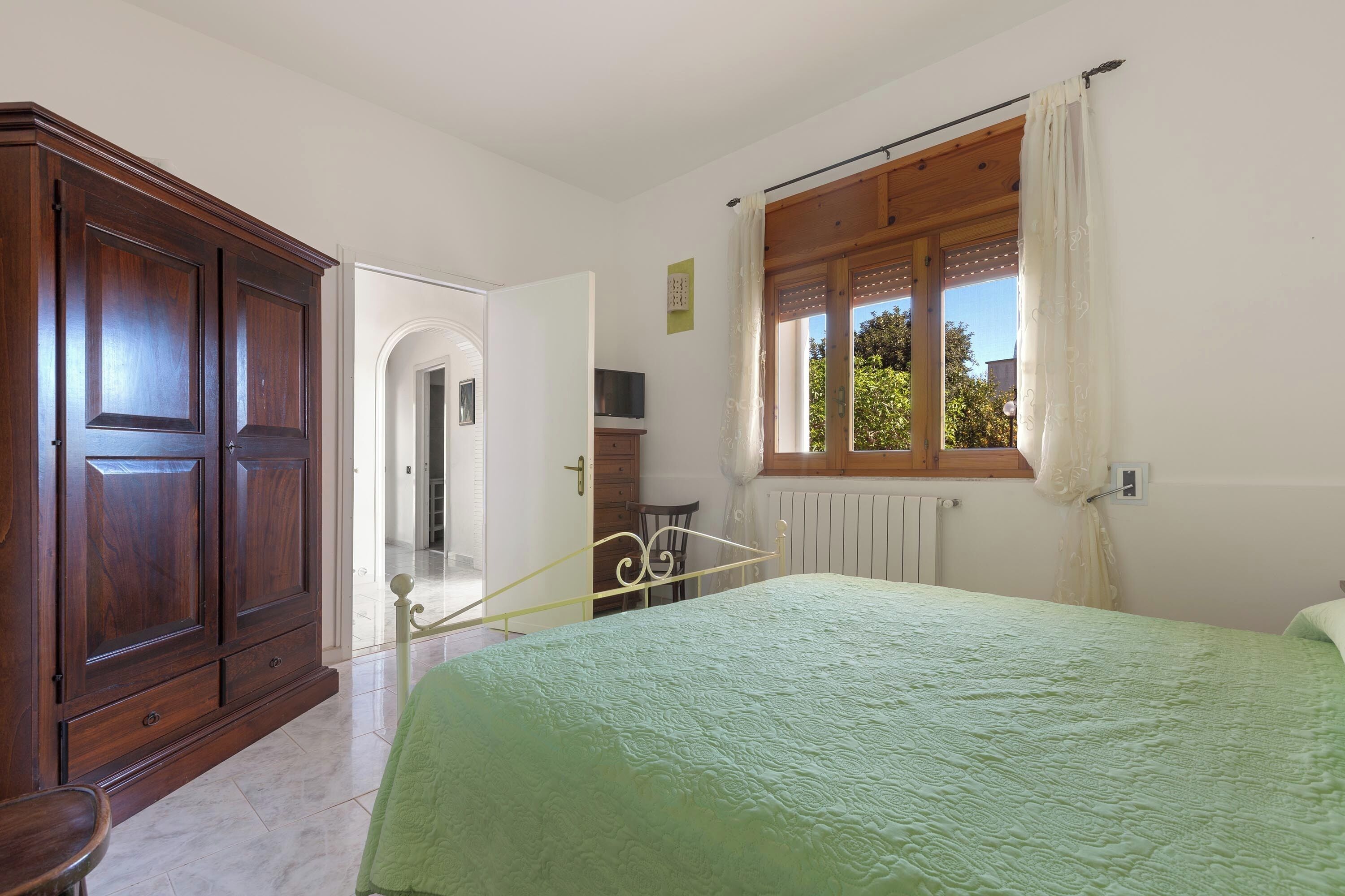 A bedroom with a bed, wooden wardrobe, and a window with curtains.