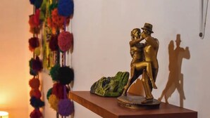 A gold statue of a man and woman on a shelf, colorful pom-poms on the wall, and a frog sculpture.