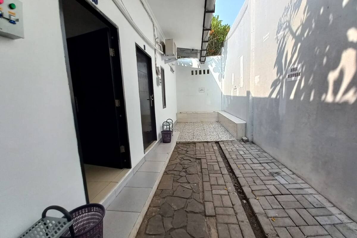 A narrow alleyway with a paved path, a black door, and a small basket on the left.