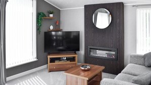 A modern living room with a flat-screen TV, a wooden coffee table, a grey sofa, and a fireplace. - 2 bedroom accommodation in Moota, near Cockermouth (Moota, near Cockermouth)