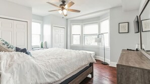 A bedroom with a large bed, a ceiling fan, a floor lamp, and a dresser.