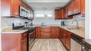 A modern kitchen with wooden cabinets, a stainless steel microwave, a gas stove, a dishwasher, and granite countertops.