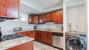 A kitchen with wooden cabinets, granite countertops, a dishwasher, a stove, and a washing machine.
