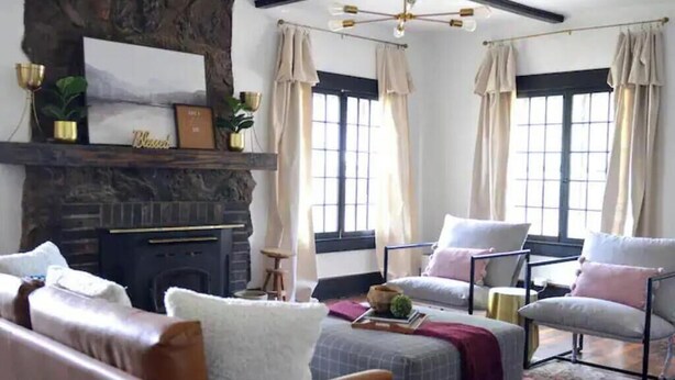 A cozy living room with a fireplace, comfortable seating, and large windows with curtains.