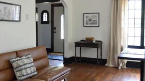 A living room with a brown leather sofa, a small table with a bowl, and a window with curtains.