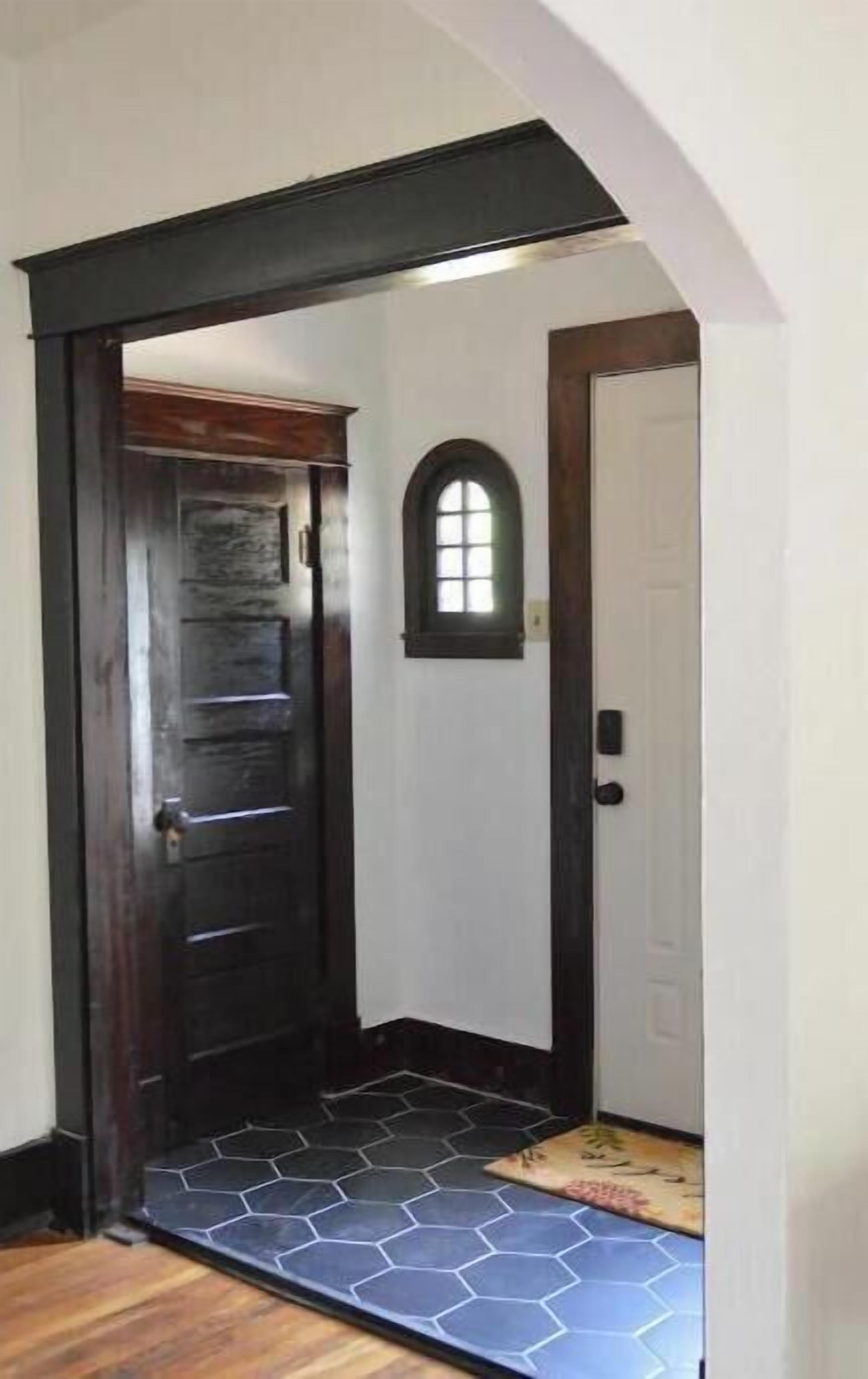 A hallway with a wooden door, a small arched window, and a tiled floor.