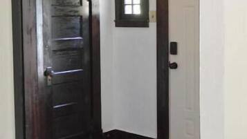 A hallway with a wooden door, a small arched window, and a tiled floor.