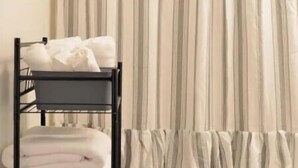 A room with a striped curtain, a black metal rack with folded towels, and a ruffled curtain at the bottom.