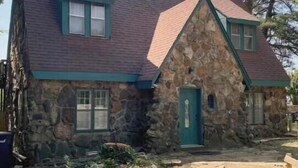 A stone house with a steeply pitched roof, a blue door, and a small porch area.