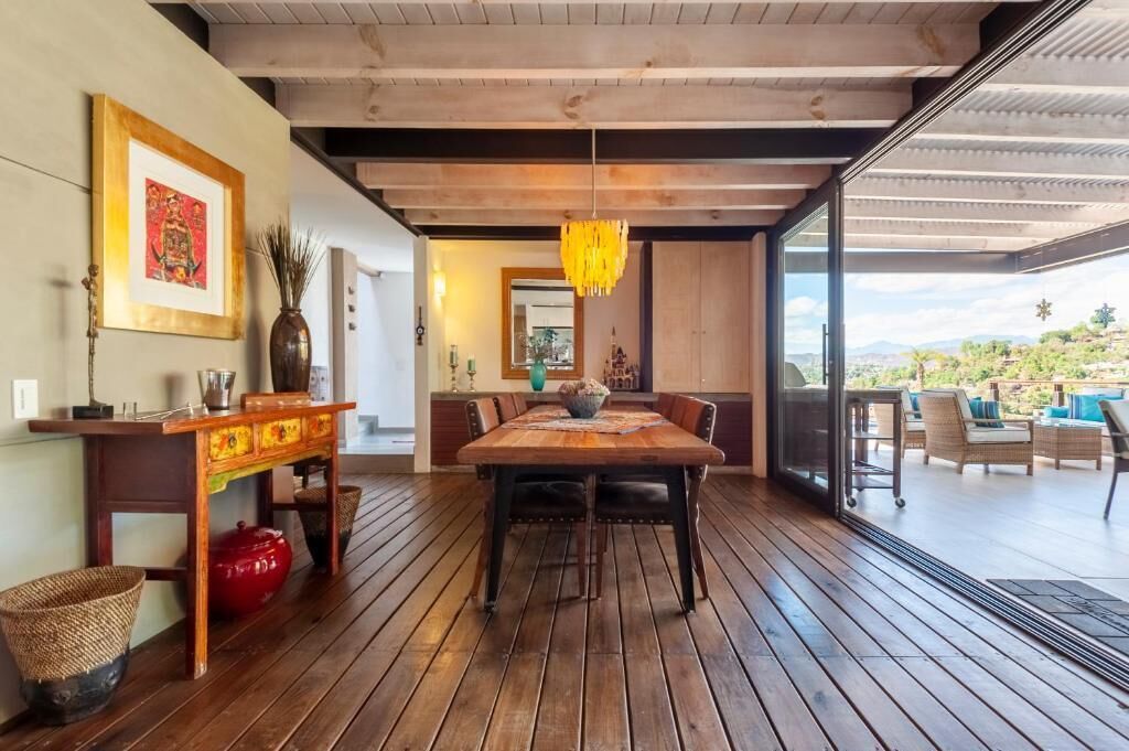 A dining area with a wooden table and chairs, a hanging light fixture, and a view of the outdoors.