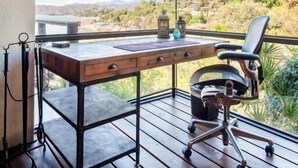 Un espace de bureau moderne avec un bureau en bois, un fauteuil de bureau noir et une vue sur un paysage vallonné grâce à de grandes fenêtres.