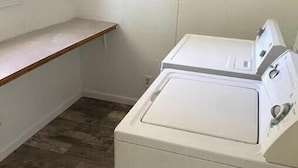 A laundry room with a washing machine and dryer, a wooden bench, and a window. - The Backyard Bungalow (Batesville)