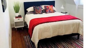 A bedroom with a bed, a nightstand, a lamp, a window, and a plant. - The Backyard Bungalow (Batesville)