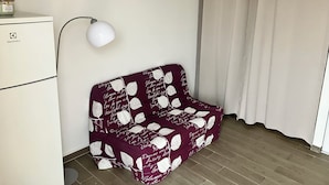 Een kleine, verzorgde kamer met een wit kastje, een witte lamp en een donkerrode bank met witte patronen.
