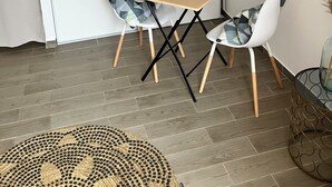 Een eetgedeelte met een houten tafel, twee witte stoelen met gestreepte kussens, een geweven placemat en een kunstwerk in een lijst aan de muur.
