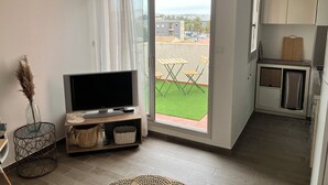 Een modern appartement met balkon, een flatscreen-tv, een eethoek met tafel en stoelen, en een keuken met kastjes en een snijplank.
