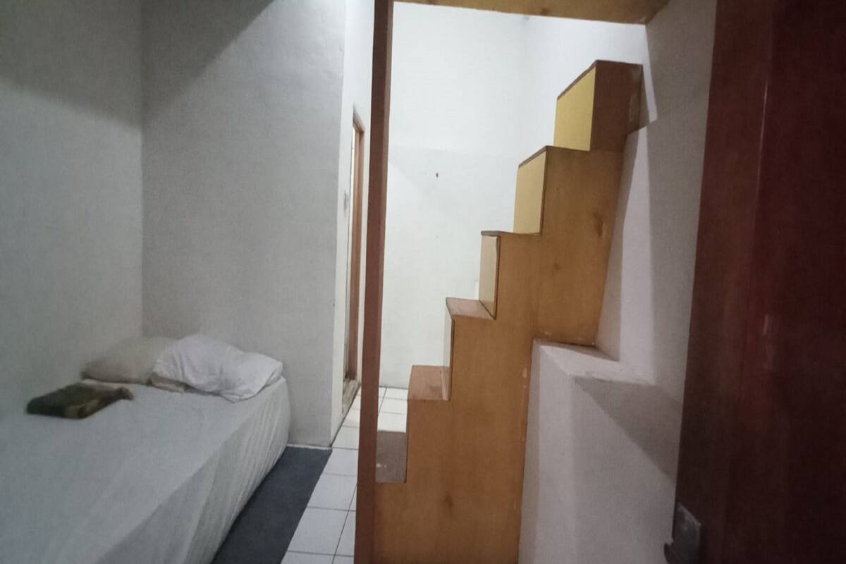 A bedroom with a bed, a wooden staircase, and a door leading to another room.