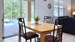 Un coin repas avec une table et des chaises en bois, une plante en pot et une vue sur une piscine, visible à travers de grandes portes vitrées.