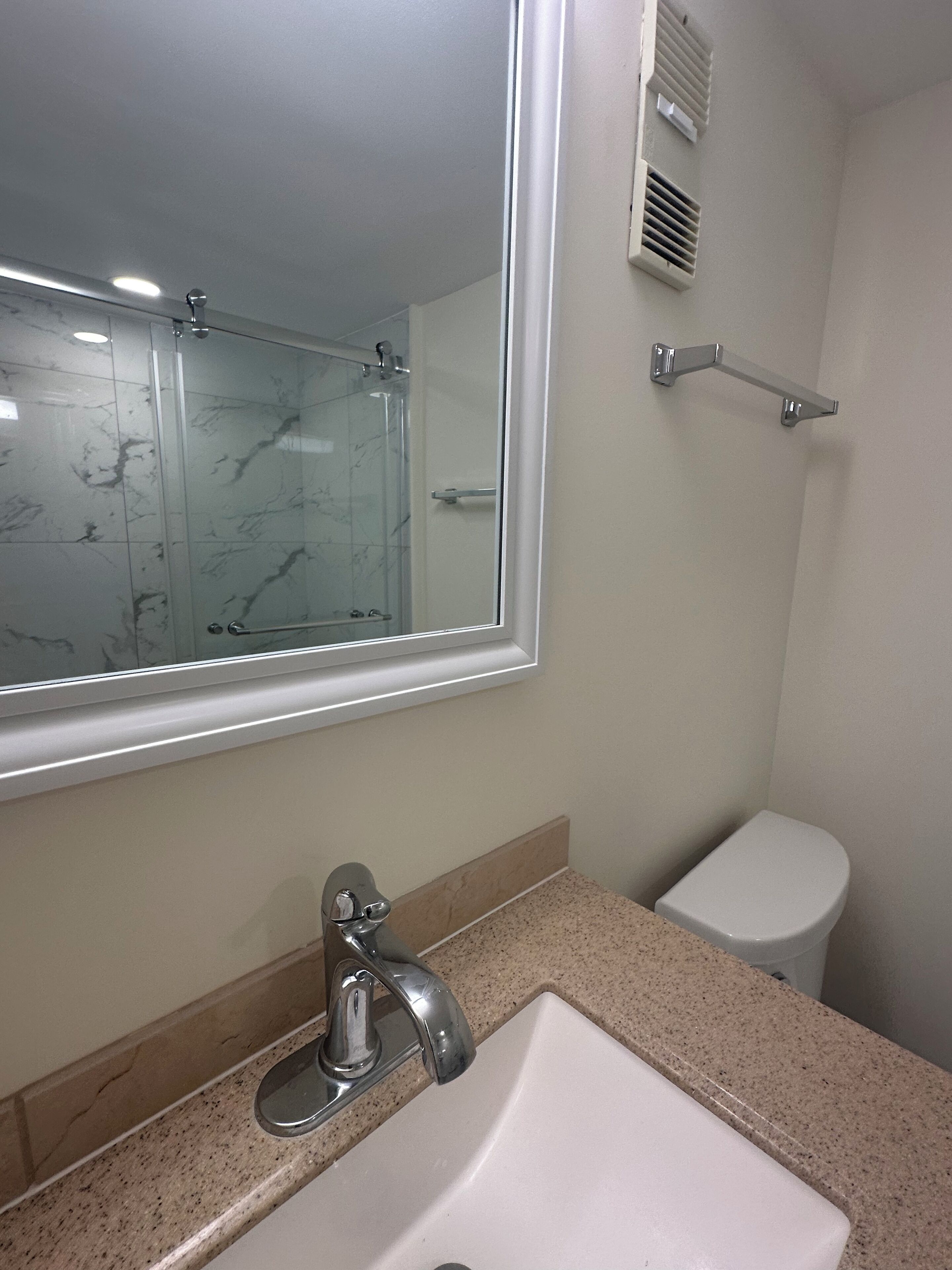 A bathroom with a marble-tiled shower, a white sink, and a toilet.