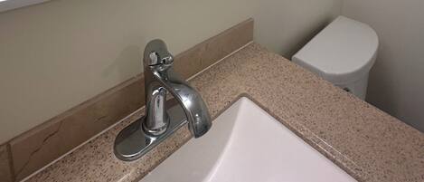 A bathroom with a marble-tiled shower, a white sink, and a toilet.