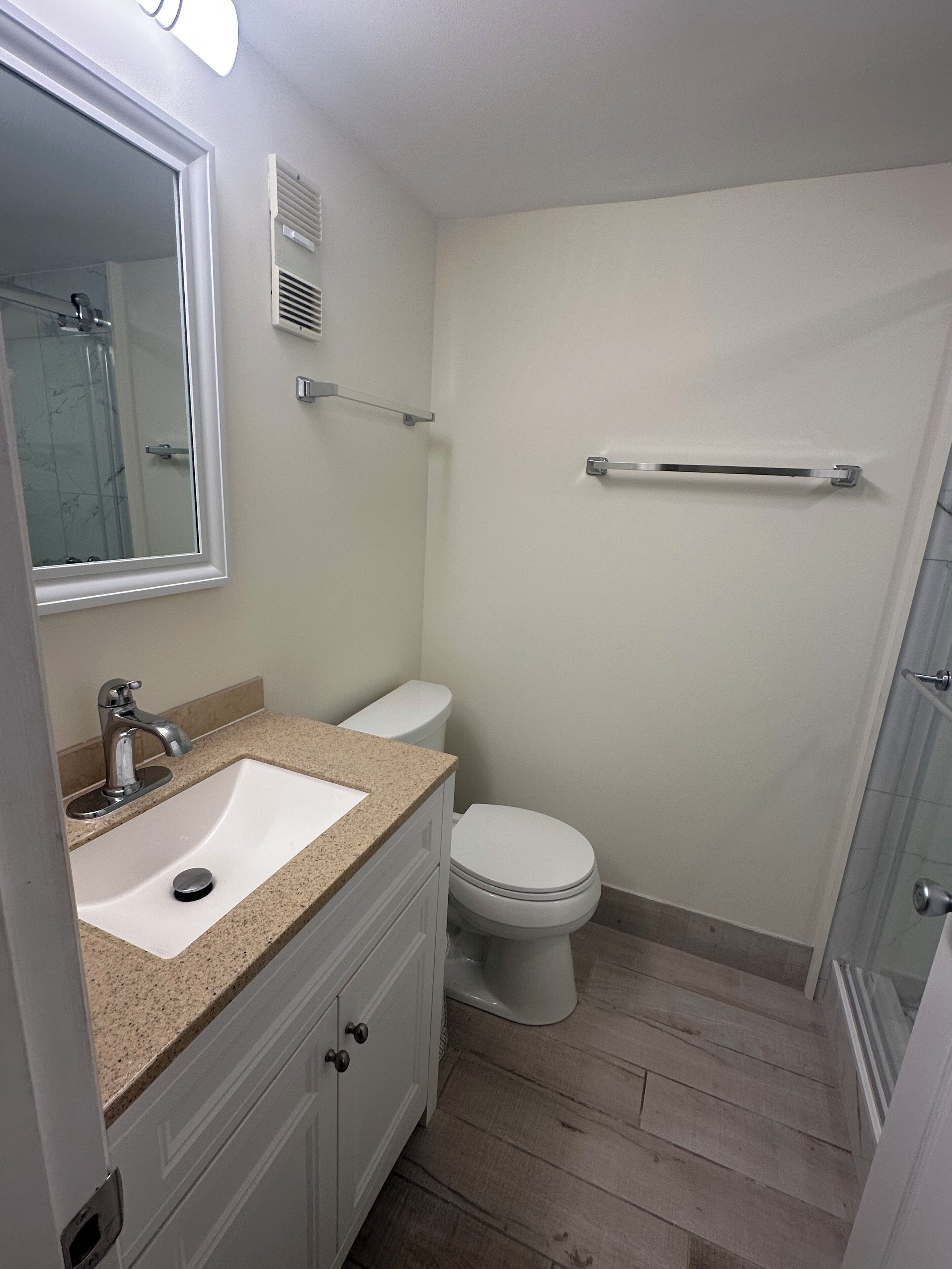 A bathroom with a white sink, a mirror, a toilet, and a shower area.