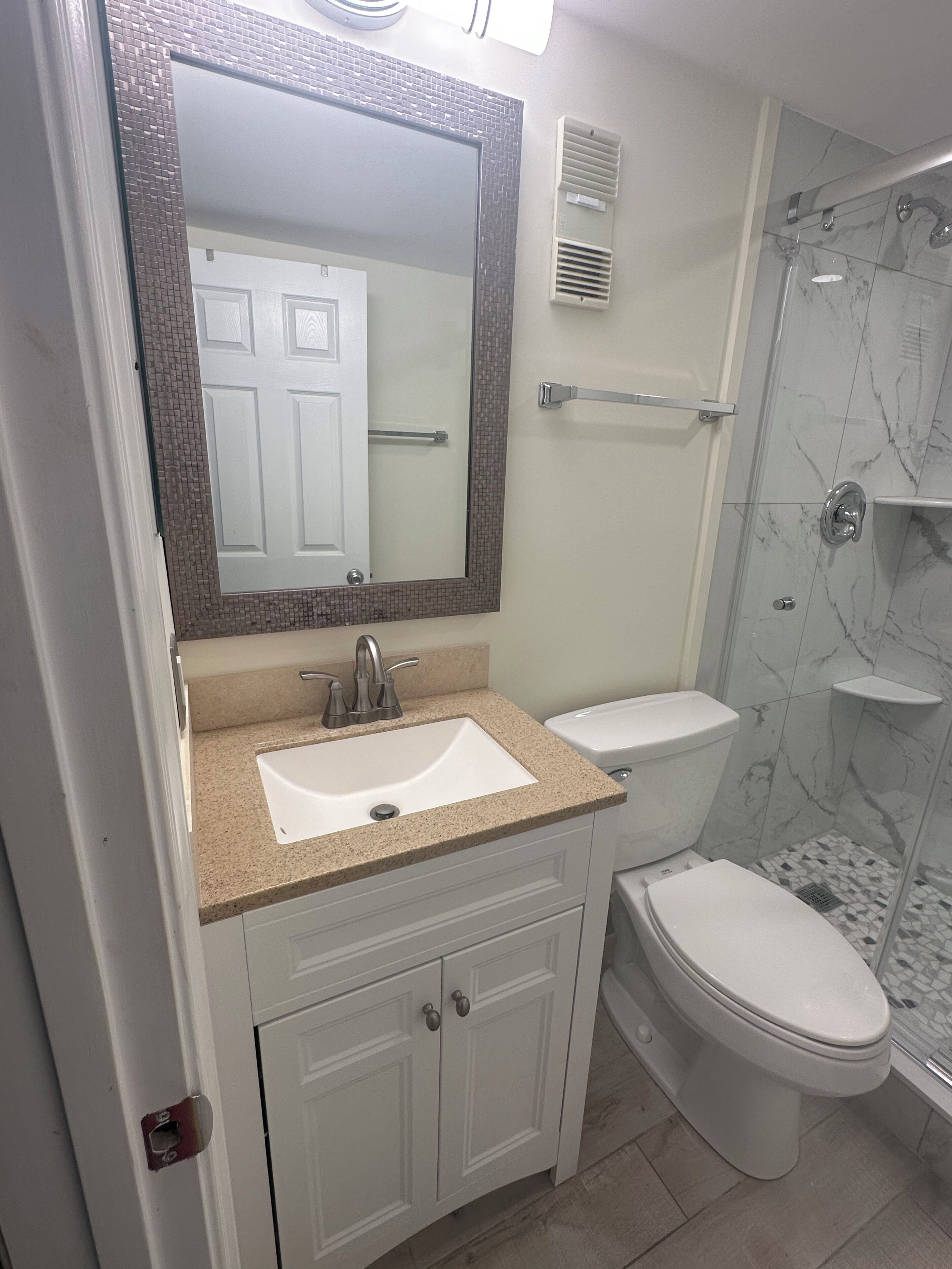 A bathroom with a white sink, a toilet, a shower with a glass door, and a mirror with a mosaic frame.
