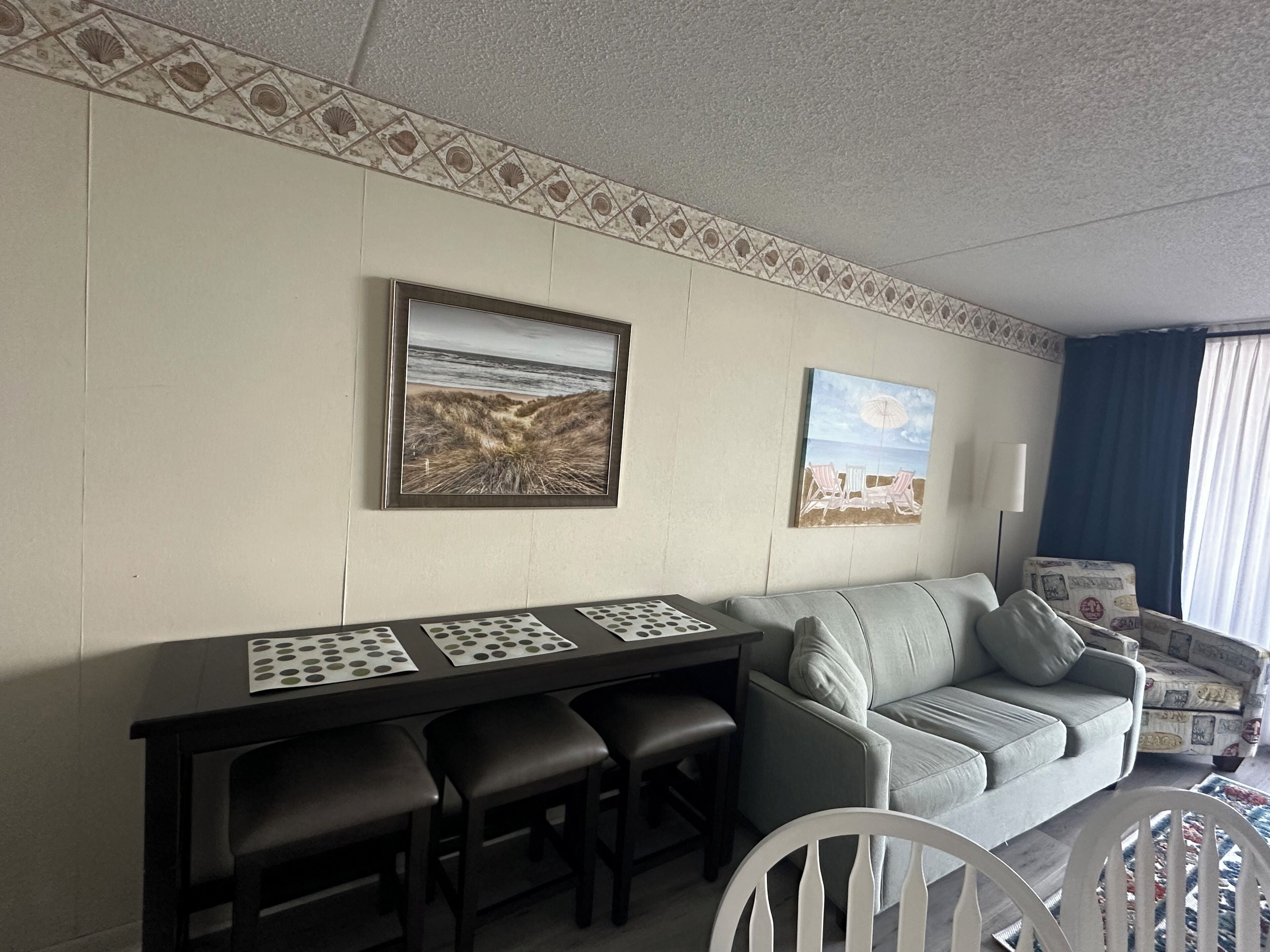 A room with a dining table, two chairs, a sofa, and a patterned wall.