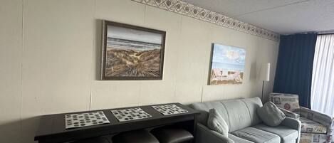 A room with a dining table, two chairs, a sofa, and a patterned wall.