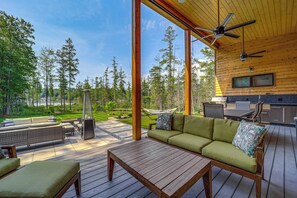 A spacious deck with a wooden table and a green sofa, a hammock, and a kitchen area with a countertop and chairs. - Chic Bellaire Home w/ Outdoor Kitchen on Clam Lake (Bellaire)