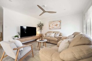 Een woonkamer met een bank, fauteuil, televisie, plafondventilator en kunst aan de muur.