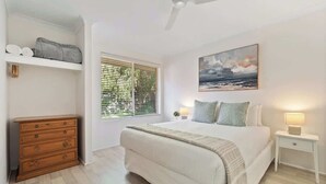 A bedroom with a bed, a dresser, a nightstand, a painting, and a window with blinds. - Luna Getaway—Spacious Family Escape by the Coast (Quindalup)