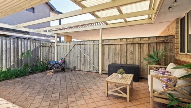 A covered patio area with a wooden fence, a table, a sofa, and a stroller. - Luna Getaway—Spacious Family Escape by the Coast (Quindalup)